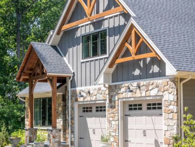 large home exterior with asphalt roofing, wooden roof peak accents, stone around garages, and an overhang