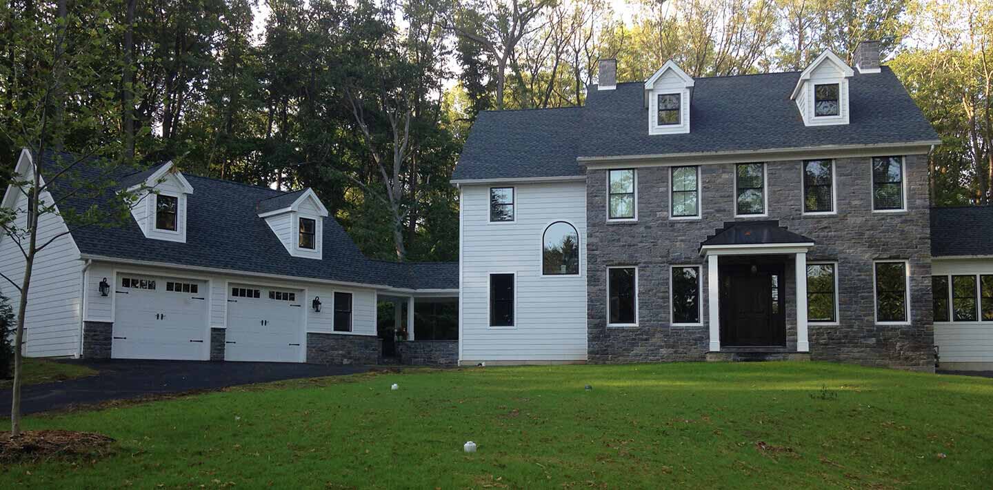 large stone and white vinyl cape cod home with attached vinyl cape cod garage